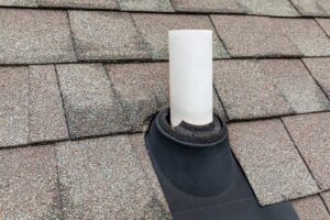 Roofing worker installs protective underlayment across a residential roof deck beside stacked shingles.